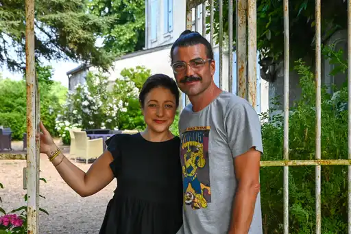 Ein junges Paar steht Arm in Arm vor dem Eingangstor eines schönen Hauses