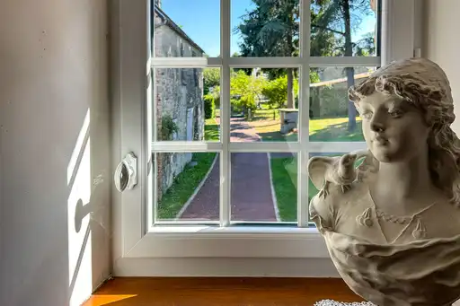 Ein Büste steht auf dem Fensterbrett vor dem Fenster mit Gartenblick in der Normandie