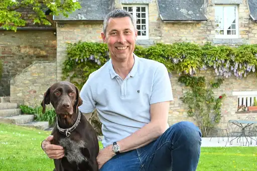 Gastgeber steht vor dem Landhaus in der Normandie mit seinem Hund