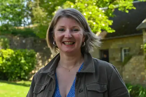 Die Gastgeberin steht lächelnd im Garten des Landhauses in der Normandie