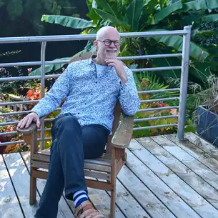 Der Gastgeber des Hauses am Flussufer in der Bretagne sitzt lächelnd auf der Terrasse 