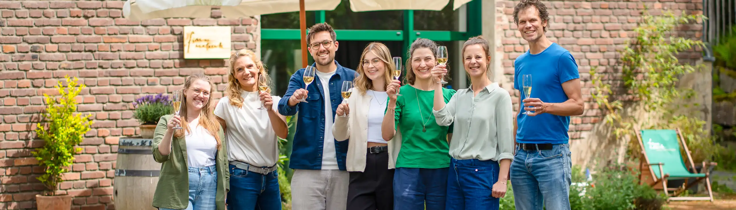 Sieben Personen mit Sektgläser vor einem Gebäude aus Backstein