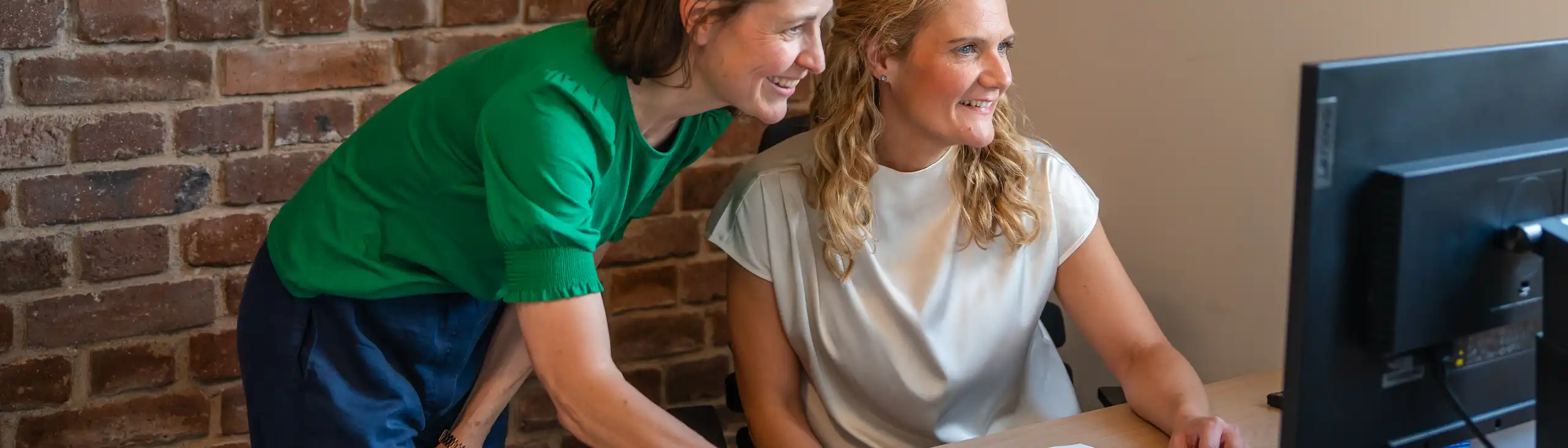 Zwei Frauen an einem Schreibtisch schauen auf einen Bildschirm