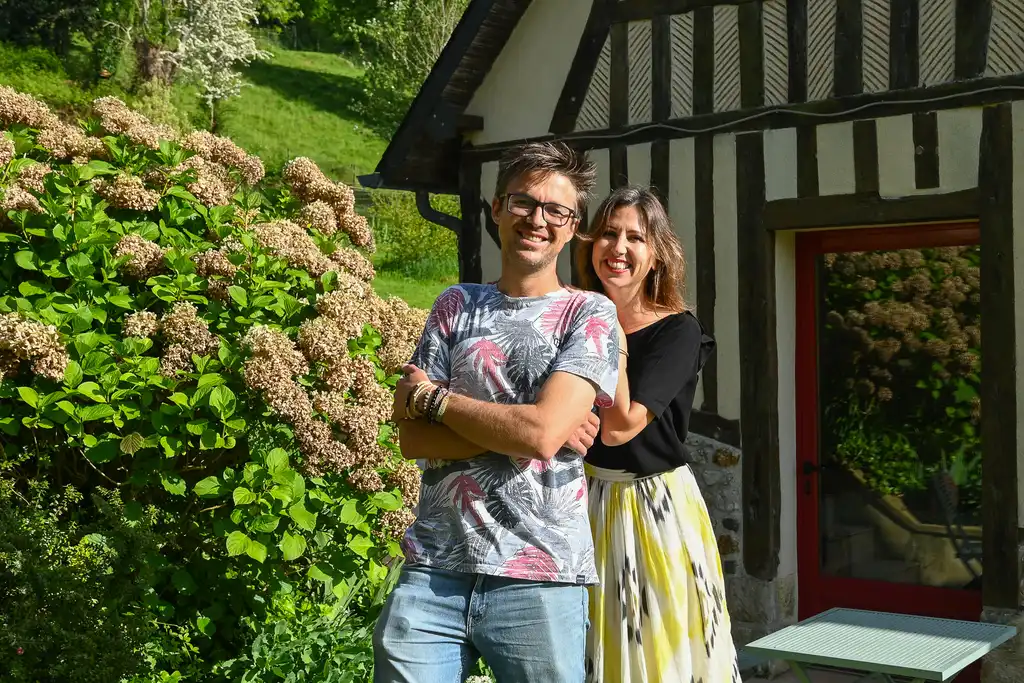 Ein Gastgeberpaar steht lächelnd vor einem Fachwerkhaus in der Normandie
