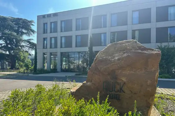 Außenansicht des modernen Ruck Hotels. Im Vordergrund ist ein Stein mit dem Namen des Hotels darauf