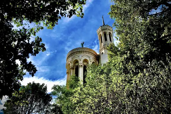 Basilika Notre-Dame de Fourvière in Lyon, man sieht nur doe Spitzen des Gebäudes hinter Bäumen aufragen 