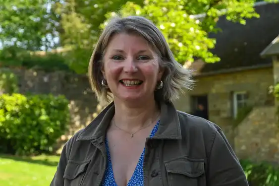 Die Gastgeberin steht lächelnd im Garten des Landhauses in der Normandie