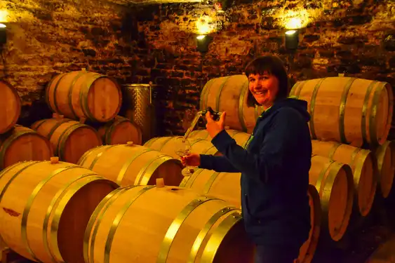 Die Winzerin begutachtet ihren Wein in einem Glas im Weinkeller zwischen Weinfässern