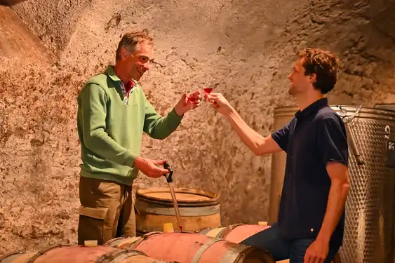 Der Gastgeber des Schlosses im Burgund und Thomas stoßen mit Wein an, im Winzerkeller.