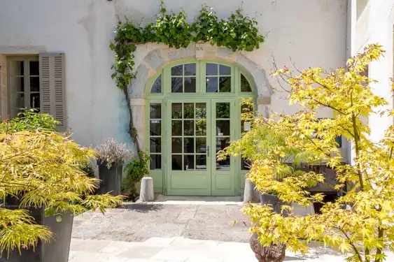 Eine grüne romantische Haustür in einem sonnenbeschienenem, blumigen Garten