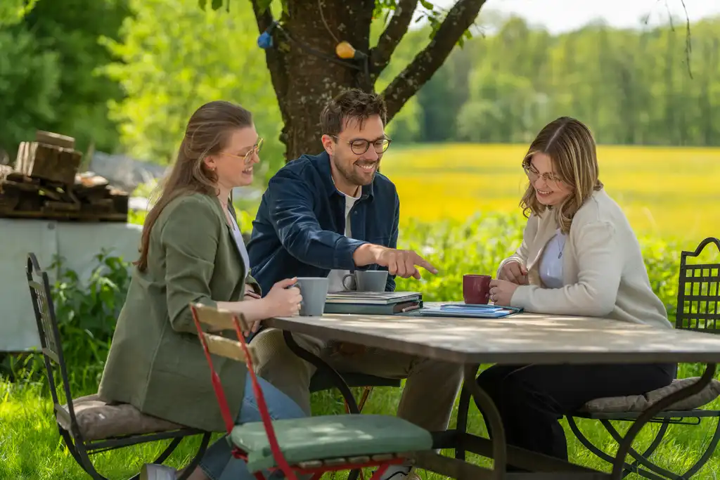 Drei Personen sitzen draußen an einem Tisch und schauen sich Reiseunterlagen an