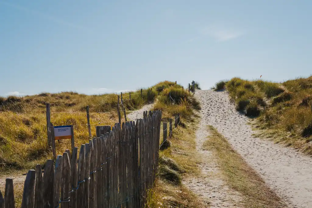 Ein Weg der über eine Düne führt in der Normandie entlang eines Holzlattenzauns