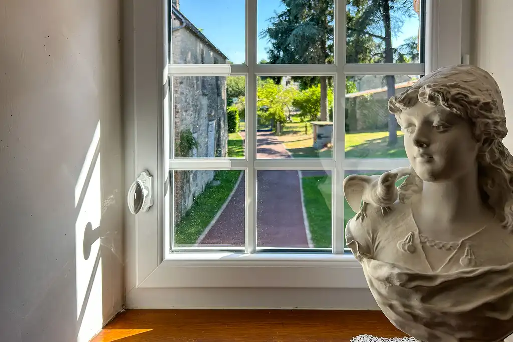 Ein Büste steht auf dem Fensterbrett vor dem Fenster mit Gartenblick in der Normandie