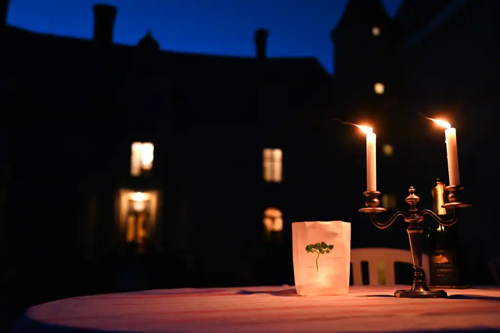 Ein Tisch im Innenhof des Schlosses im Burgund auf dem ein Kerzenhalter und eine Lichttüte stehen und leuchten
