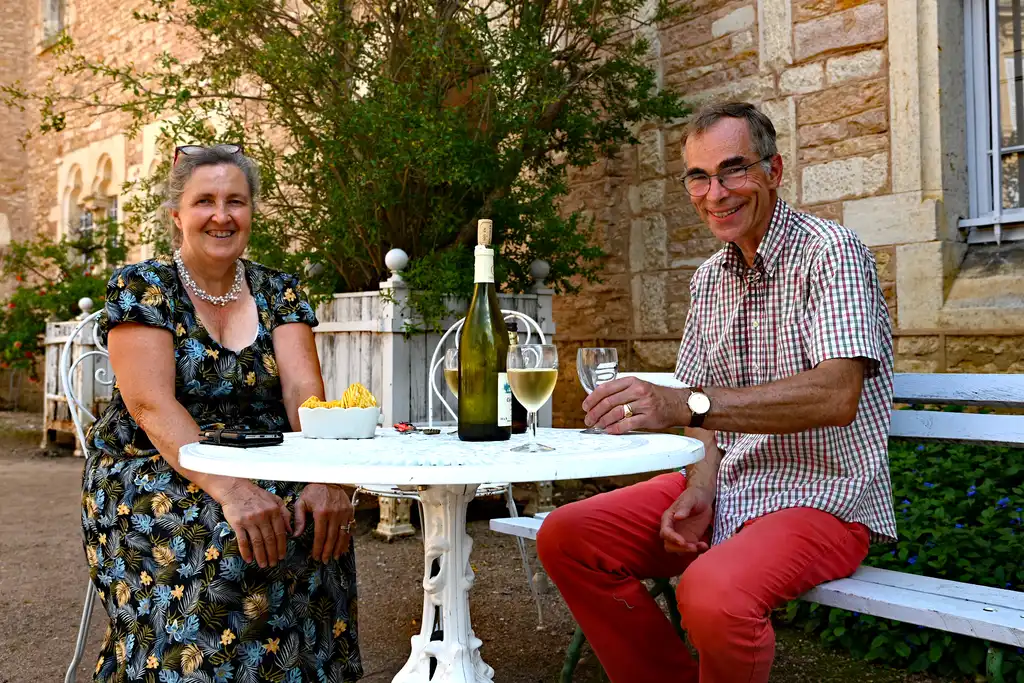 Das Gastgeberpaar des Schlosses im Burgund sitzt am Tisch im Garten und genießt ein Glas Wein