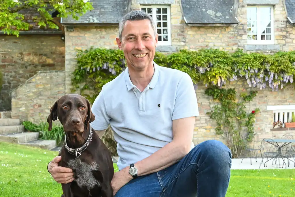 Gastgeber steht vor dem Landhaus in der Normandie mit seinem Hund