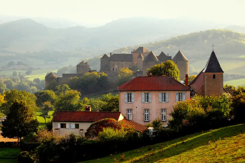 Eine Burg im Burgund mit großen Bergen im Hintergrund und leichtem Nebel