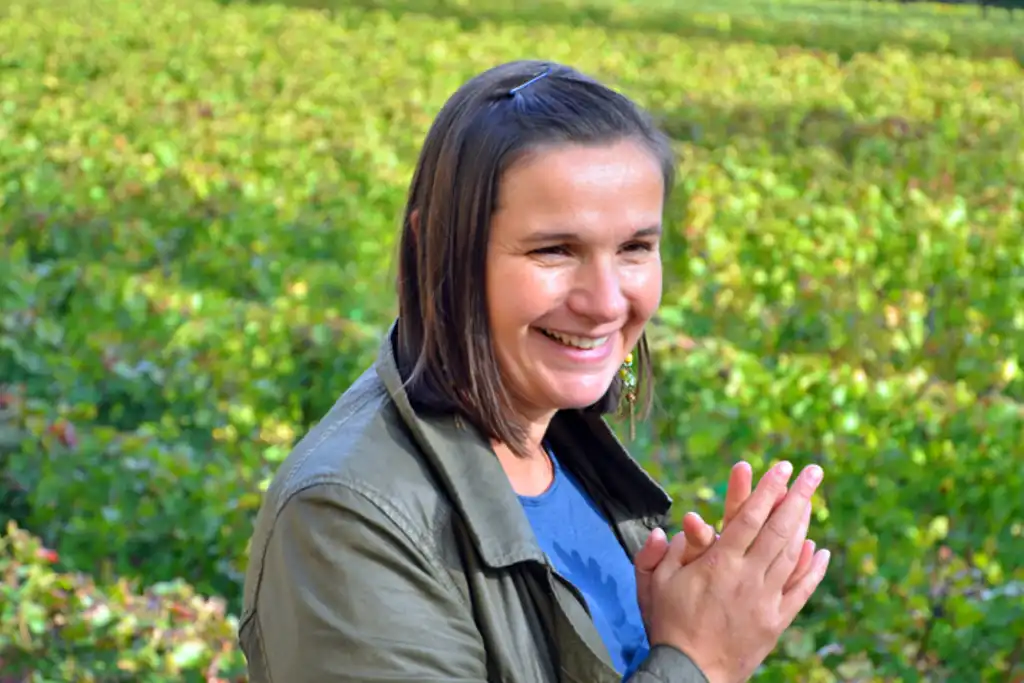 Eine Frau steht lächelnd zwischen Weinreben im Burgund