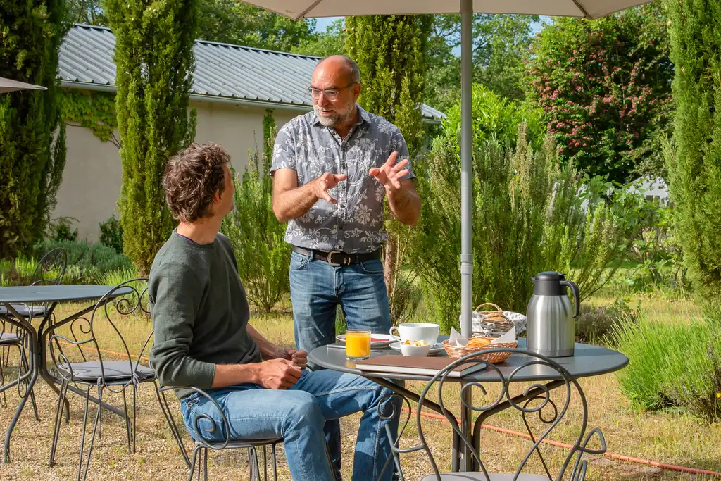 Thomas und der Gastgeber besprechen etwas beim beim Frühstück im Garten des Gutshofs in der Loire