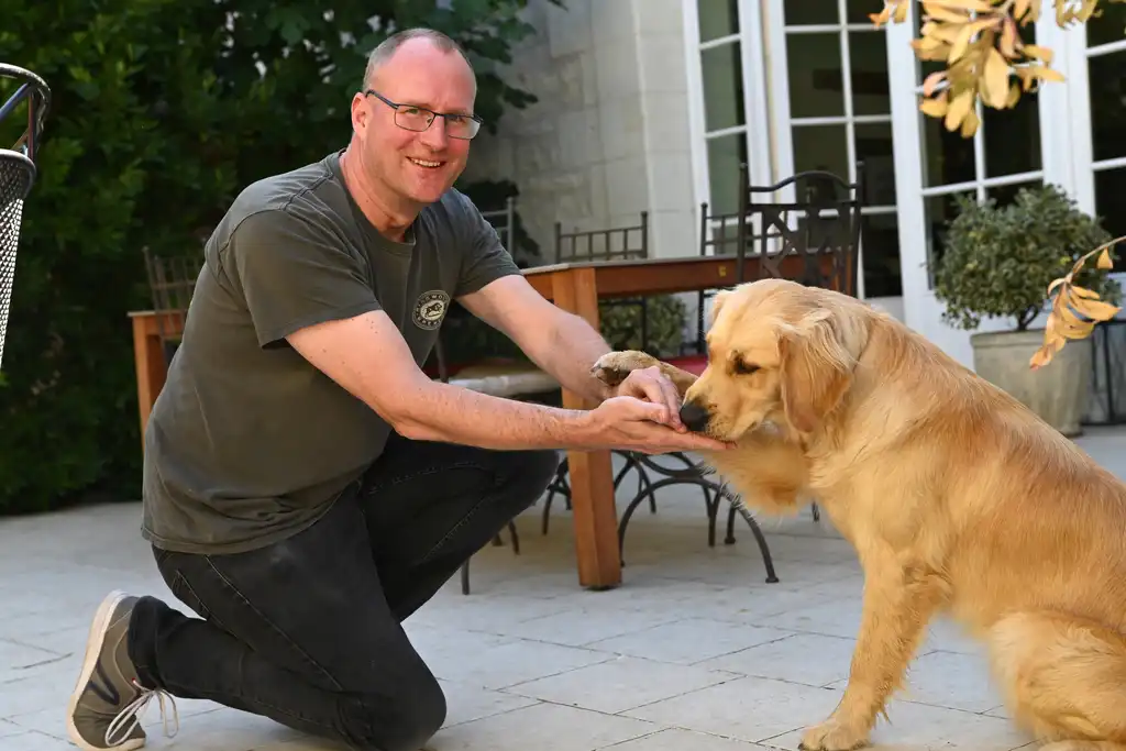 Der Gastgeber des Tuffsteinhauses in der Loire sitzt auf der Terrasse mit seinem Hund und hält seine Pfote