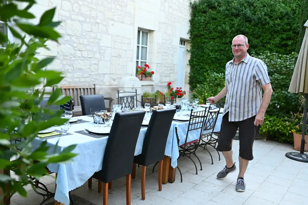 Der Gastgeber des Tuffsteinhauses in der Loire steht auf der Terrasse neben dem gedeckten Esstisch