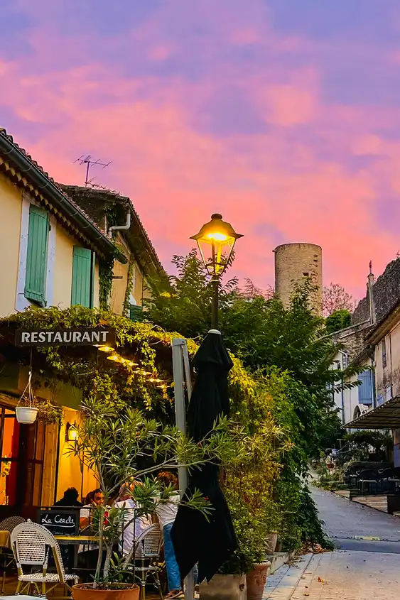 Eine Straße in einem Dorf der Provence mit einem charmanten Restaurant und einem vom Sonnenuntergang gefärbten Himmel