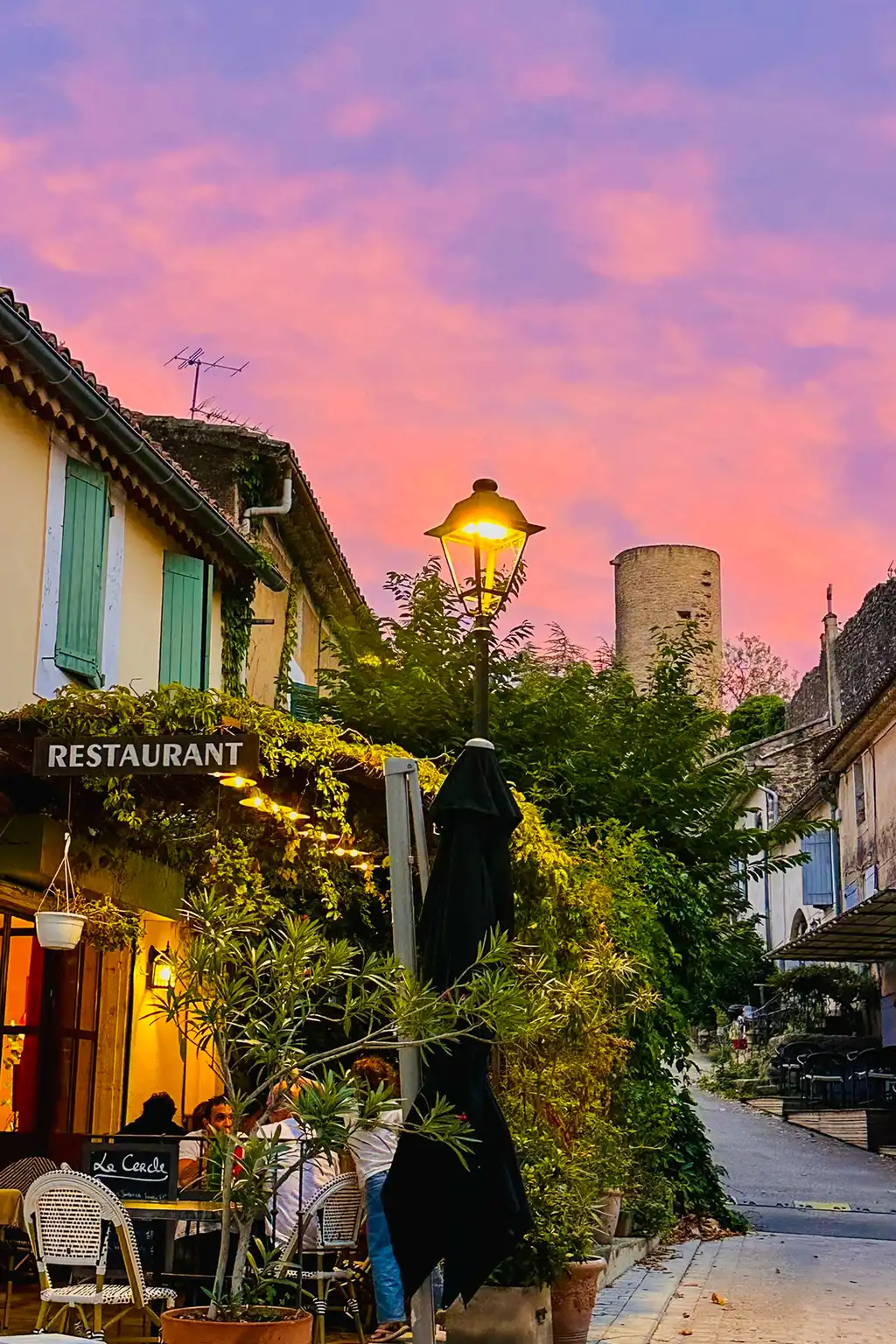 Eine Straße in einem Dorf der Provence mit einem charmanten Restaurant und einem vom Sonnenuntergang gefärbten Himmel