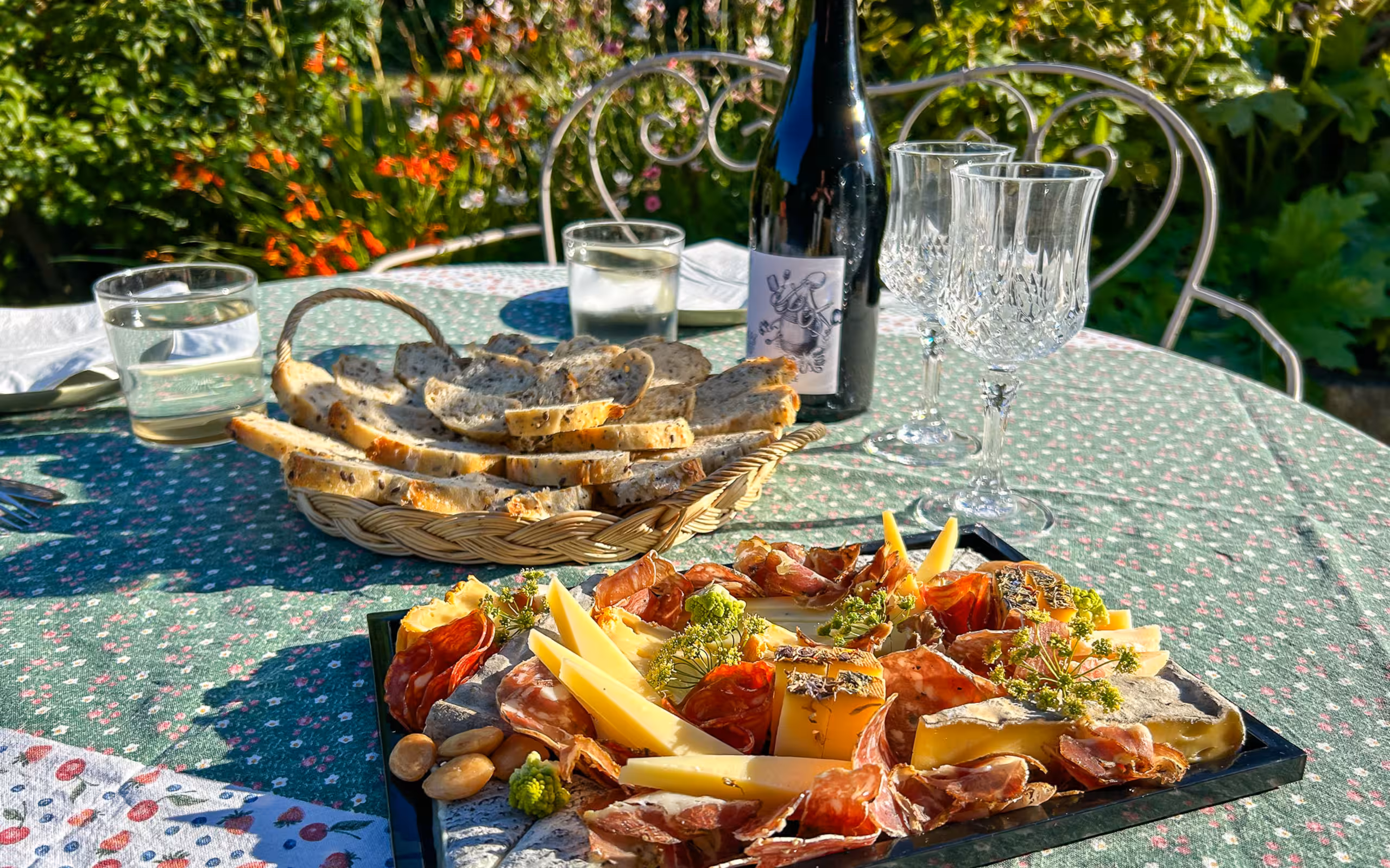 Eine Picknickplatte auf einem Tisch mit grüner Tischdecke, einem Brotkorb und einer Flasche Wein