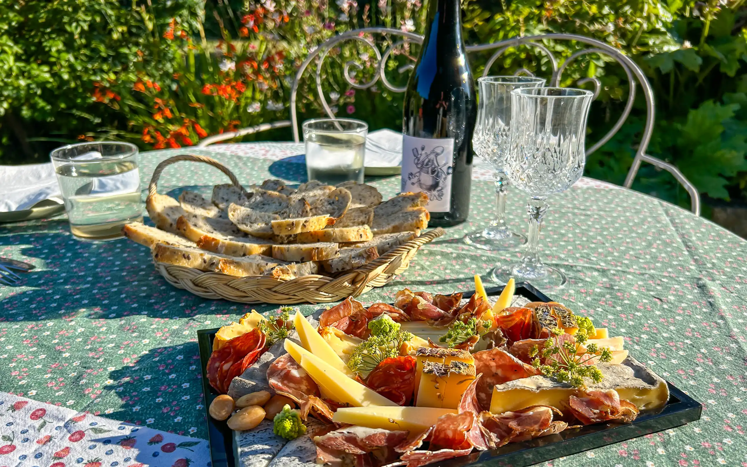 Eine Picknickplatte auf einem Tisch mit grüner Tischdecke, einem Brotkorb und einer Flasche Wein