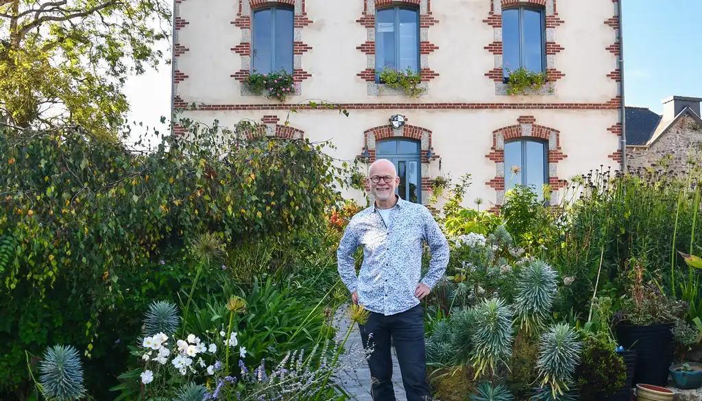 Der Gastgeber des Hauses am Flussufer in der Bretagne steht herzlich lächelnd vor dem Haus