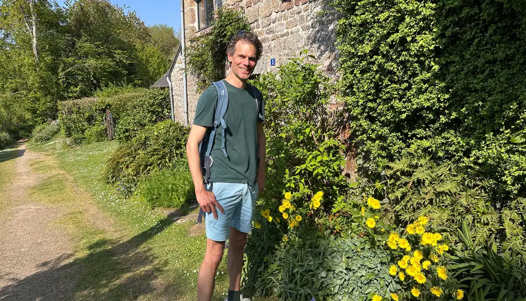 Thomas steht vor einem Steinhaus in der Normandie